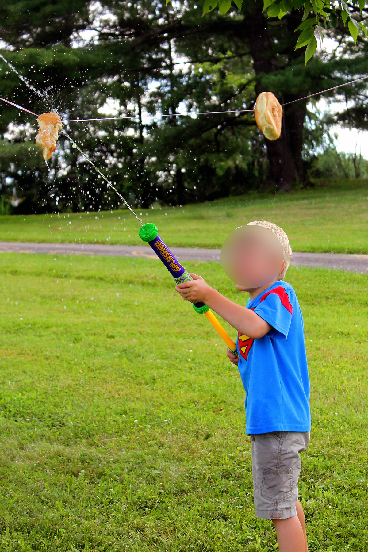 Young boy in a Superman shirt blasting a soggy hamburger bun off a clothesline with a water blaster during Bun Blasters game.