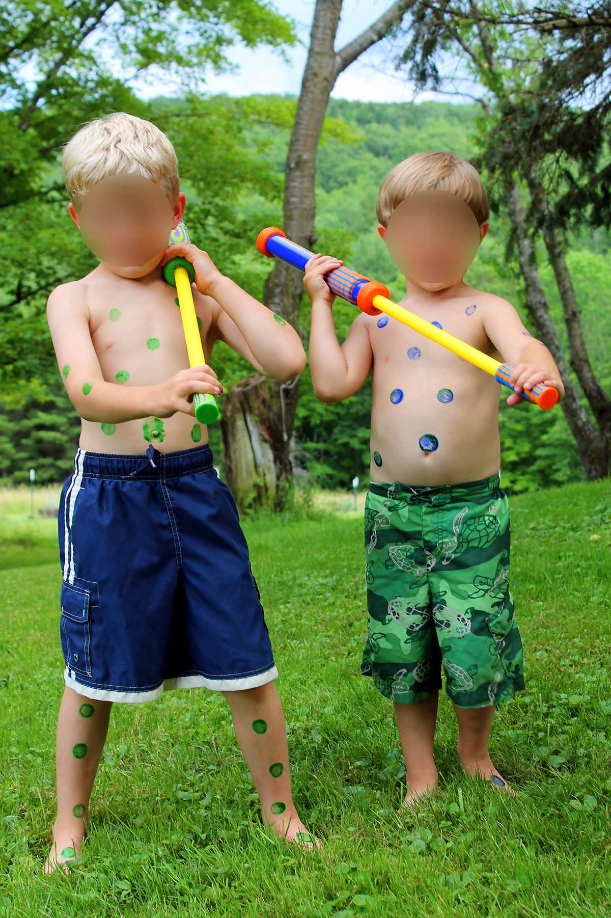 Two boys covered in green and blue paint dots standing in a backyard holding water blasters ready to play Dot Blaster Wars.