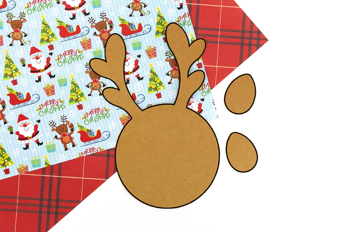 Cutting out a printed reindeer template with scissors on a craft table.