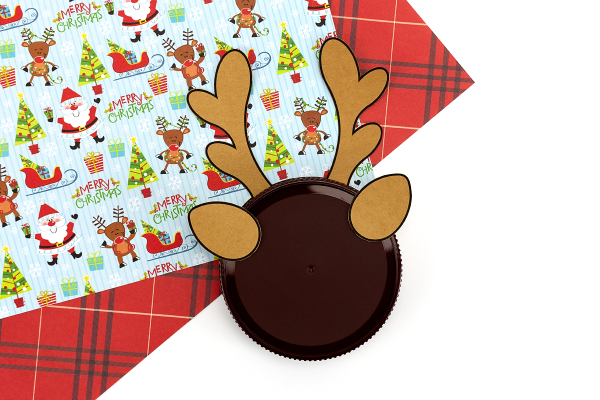 Gluing brown ear pieces to the top of the jar lid to form the reindeer shape.