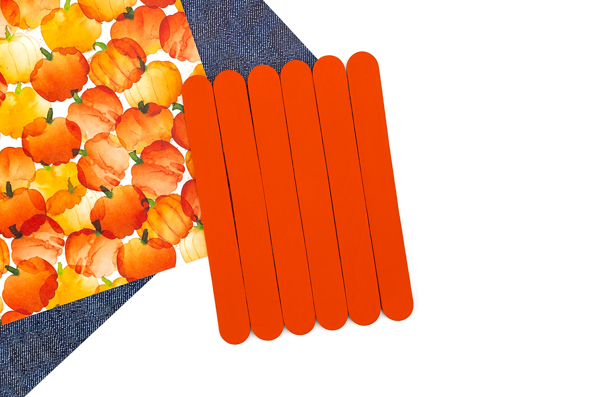 Painting a popsicle stick pumpkin orange for a fall keepsake craft.