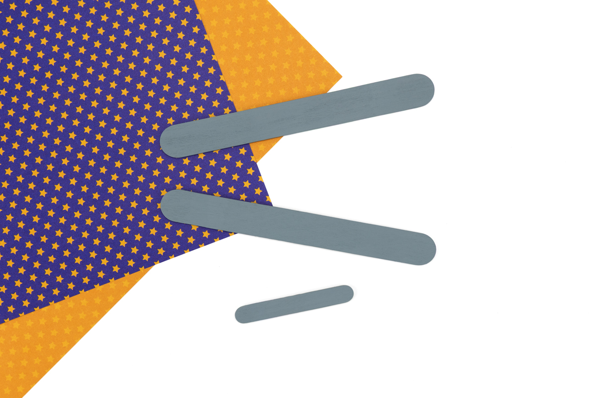 Wide and miniature craft sticks painted grey and drying on a flat surface.