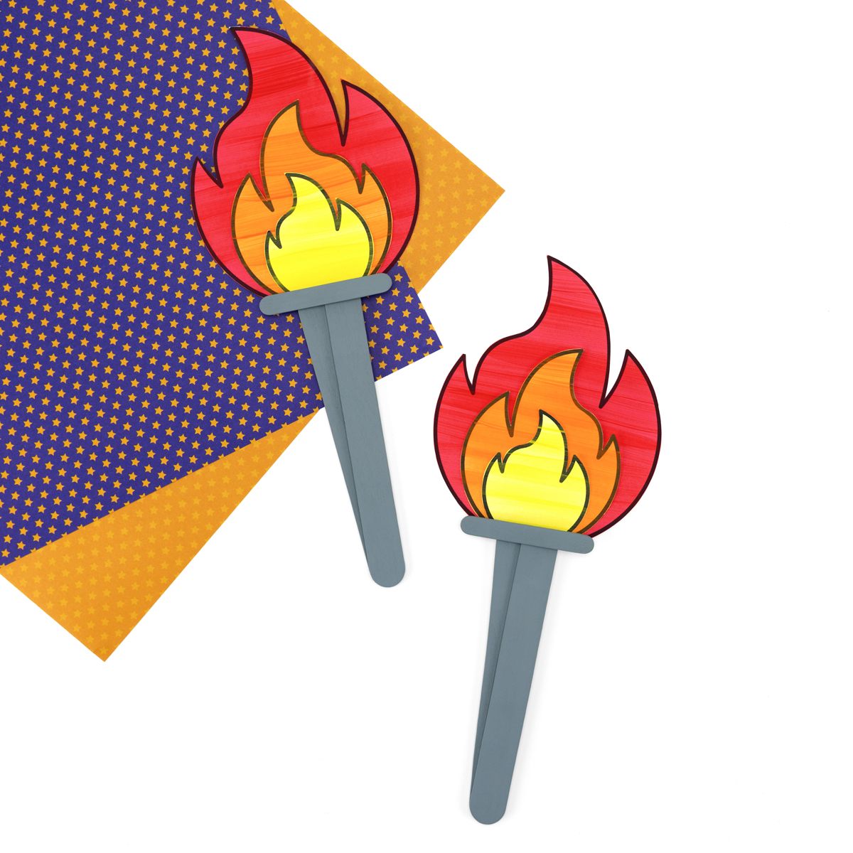 Completed paper and craft stick torch with layered red, orange, and yellow flames, standing upright on a flat surface.