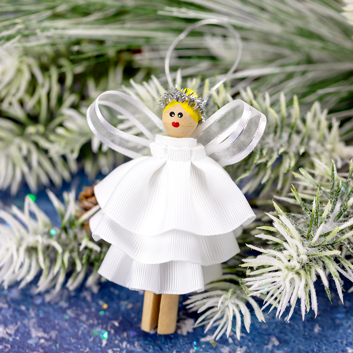 DIY Clothespin Angel Ornament A completed clothespin angel ornament with blond hair, painted face, white ribbon dress, and silver halo, ready to hang on the Christmas tree.