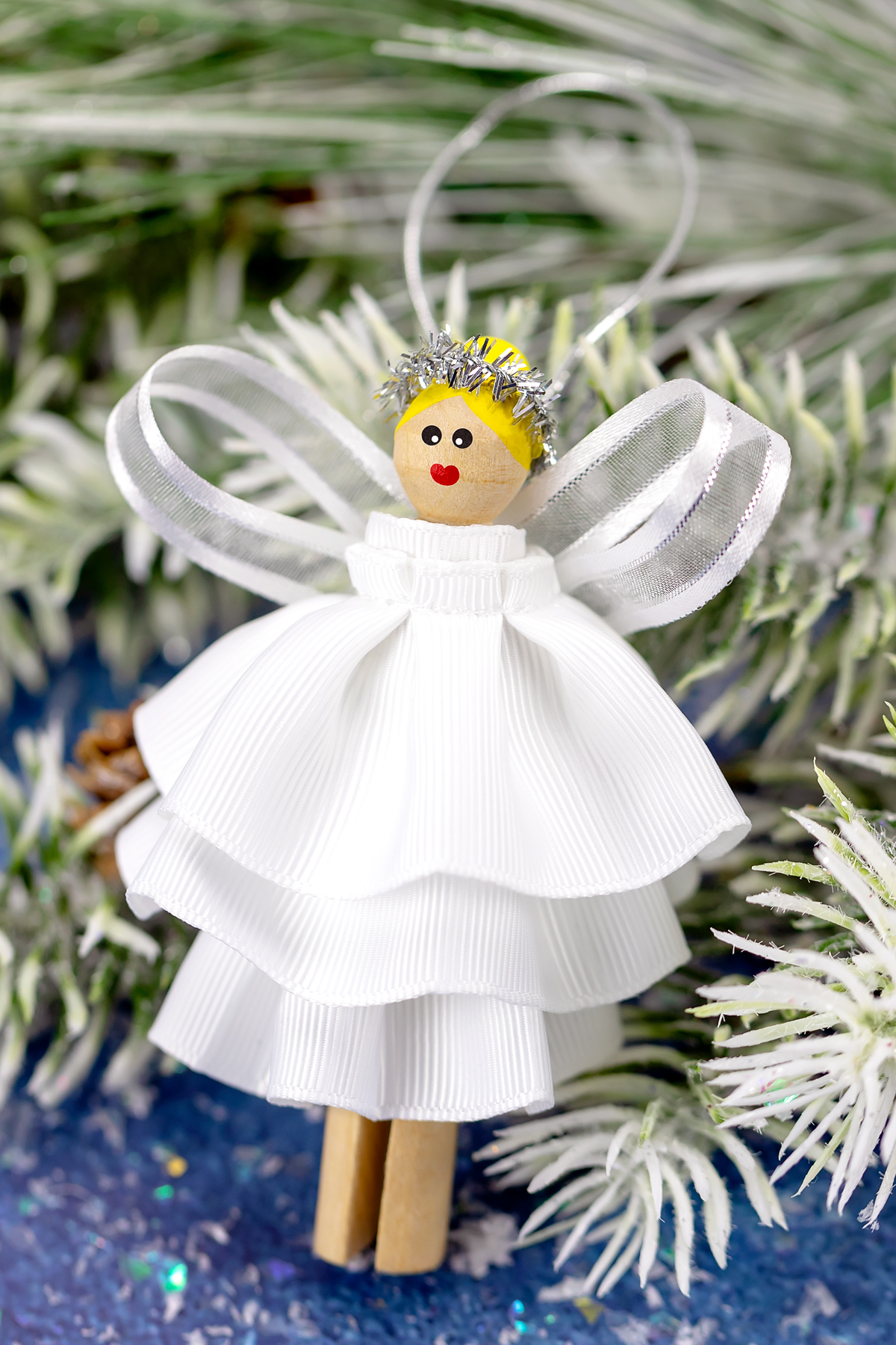 How to Make a Beautiful DIY Christmas Angel Ornament for Kids Another view of a finished clothespin angel ornament with blond hair, painted face, white ribbon dress, and silver halo, perfect for Christmas decorating.