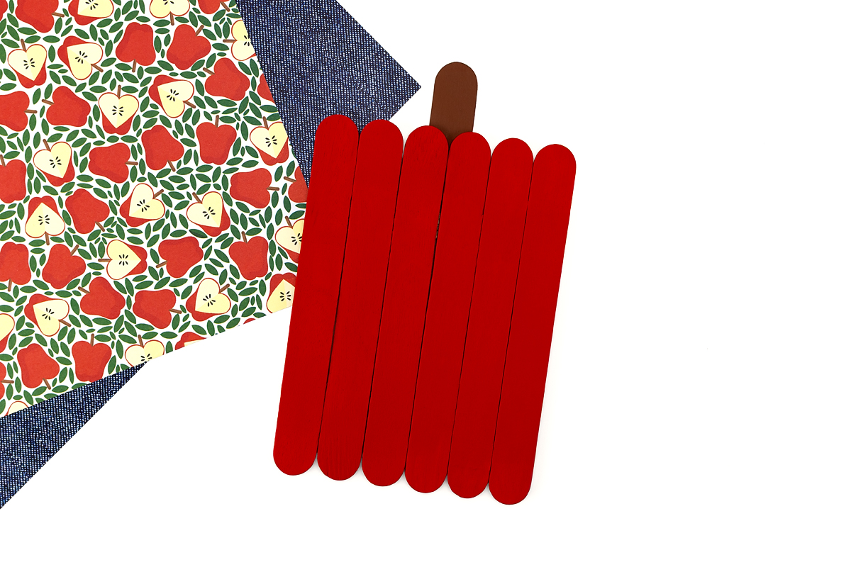 Red painted popsicle sticks with a brown stem glued to the top, an in-progress step of the popsicle stick apple craft.