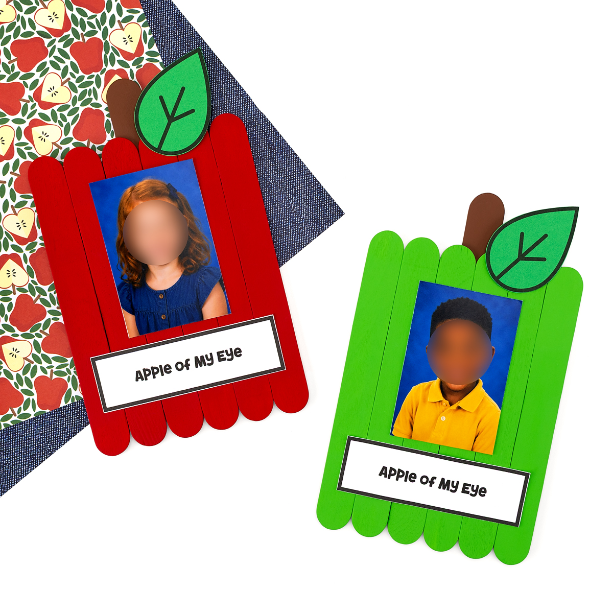 Two finished popsicle stick apple crafts, one red and one green, each with a child's photo and an Apple of My Eye label, displayed on apple print paper.