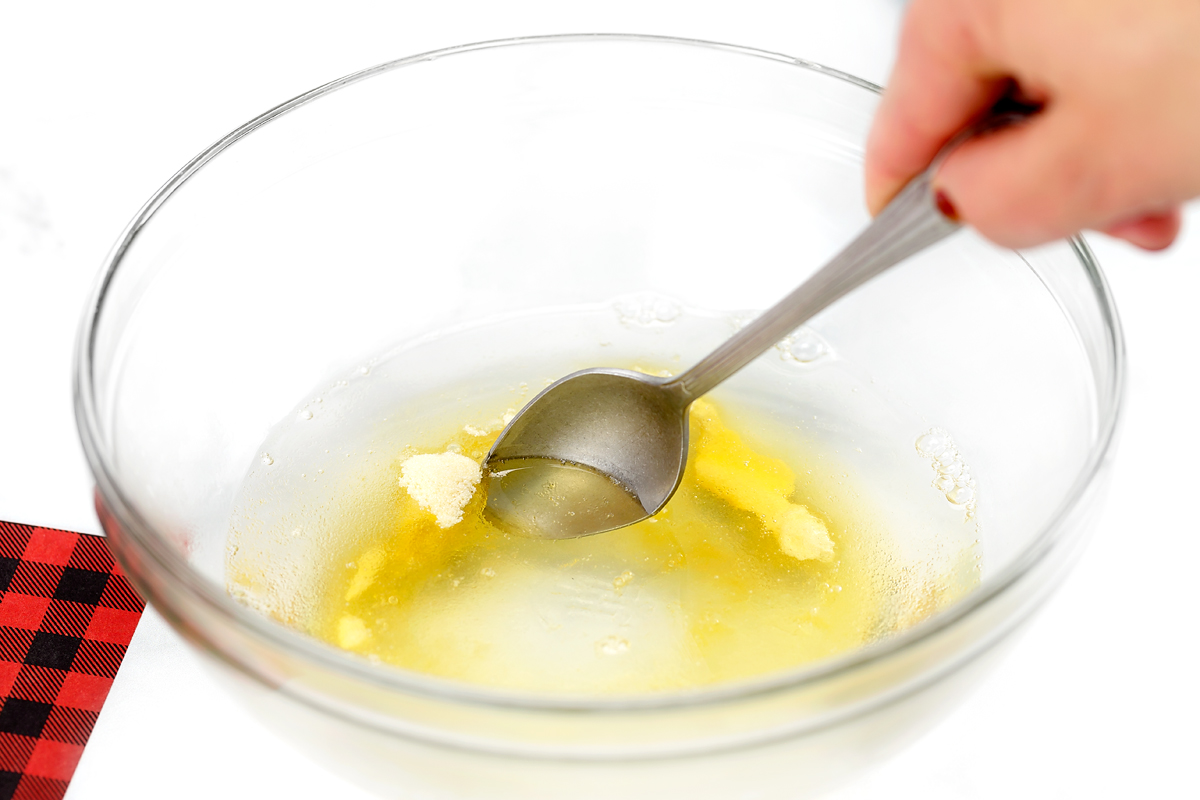 A clear glass mixing bowl containing unflavored gelatin being stirred in hot water, ready to add birdseed.