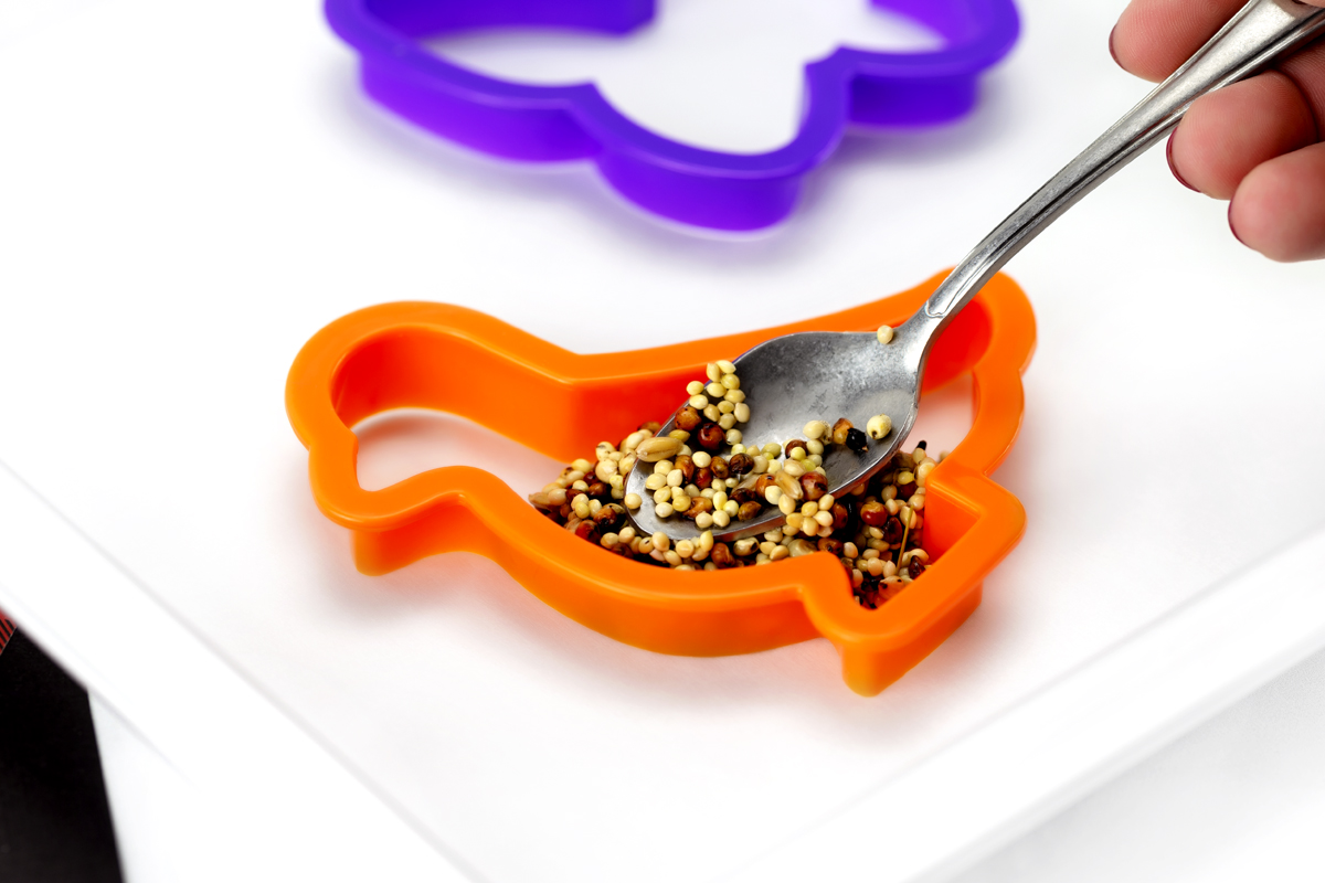 Close-up of cookie cutters partially filled with birdseed mixture on parchment paper.