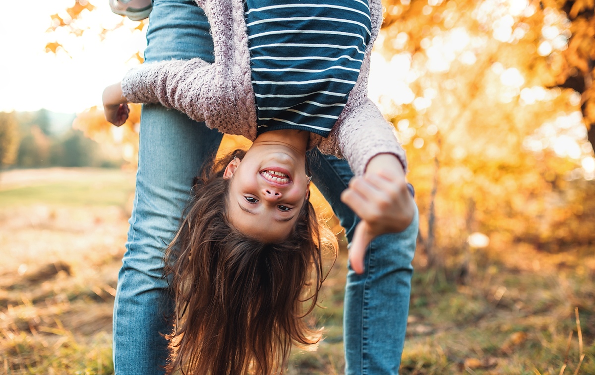 Mother swinging her daughter around outdoors. 
