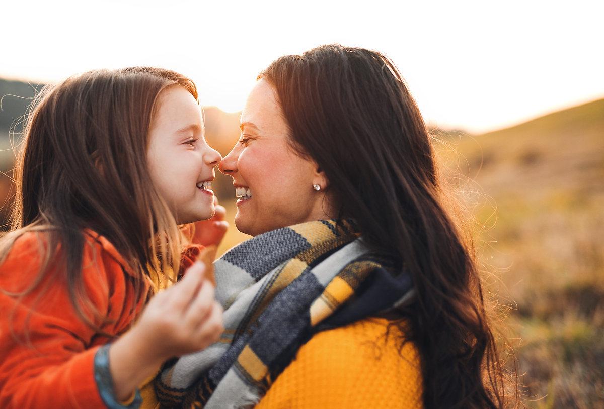 Mother and daughter laughing and sharing affection outdoors. 