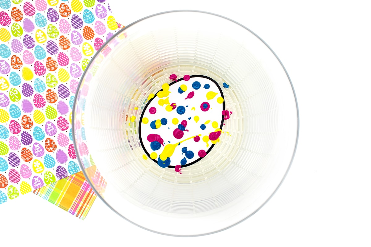 Magenta, yellow, and blue paint dripped onto a paper egg.