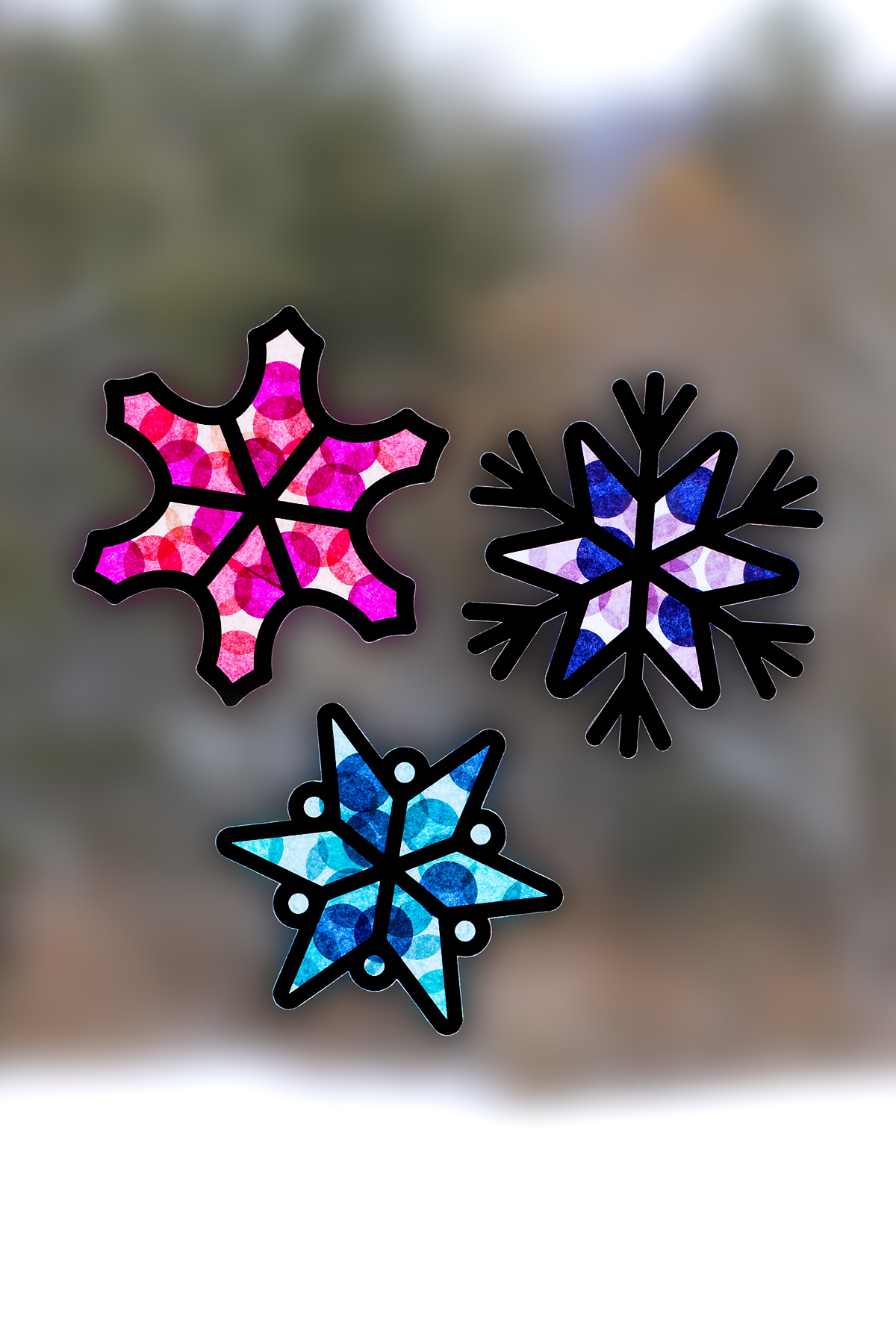 Three colorful snowflake suncatchers hanging on a window.