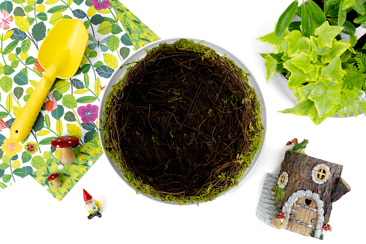 Supplies needed to make a fairy garden include soil, basket, plants, and resin miniatures.