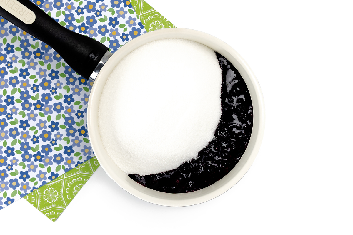Sugar and cooked blueberries in a pot.