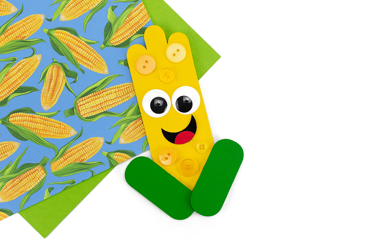 Popsicle stick corn craft with face and buttons.