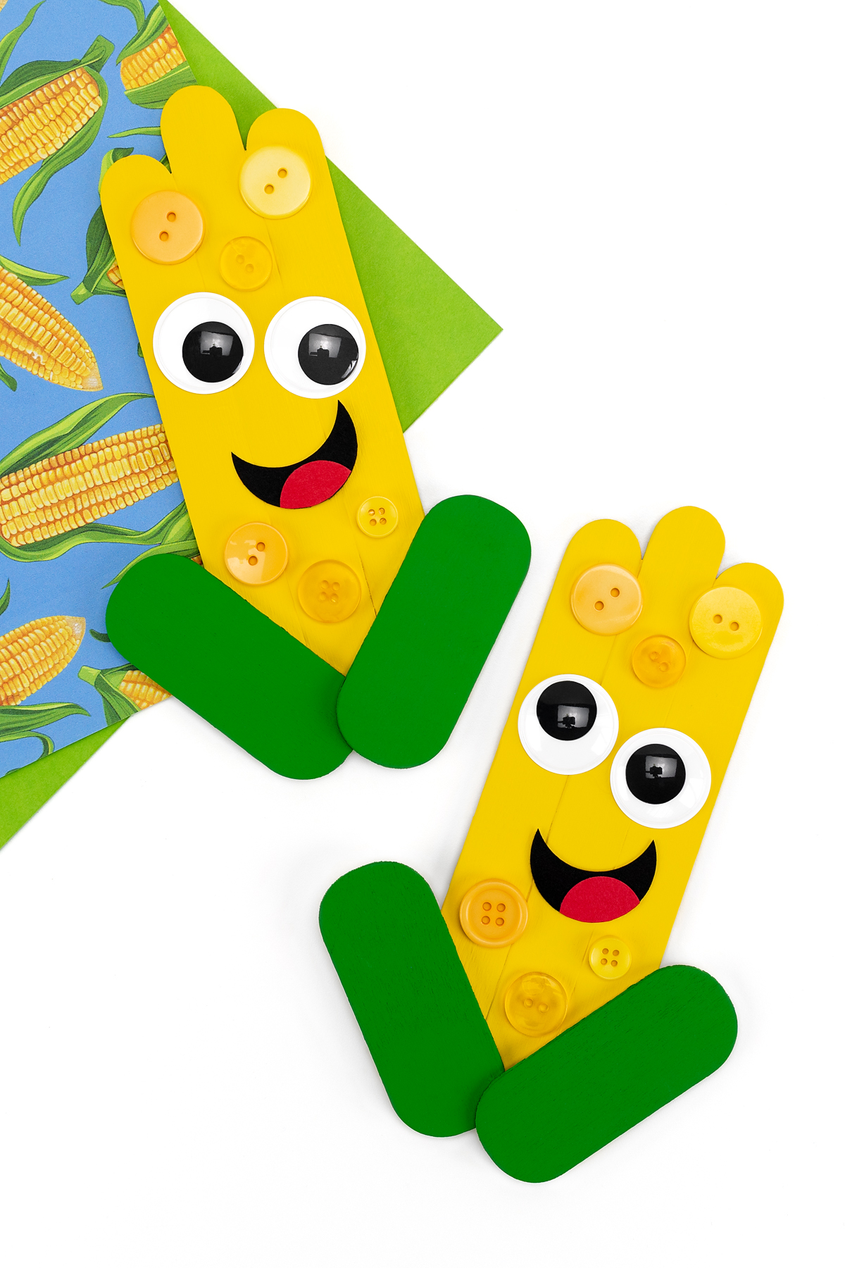 Two finished popsicle stick corn crafts with button corn kernels.