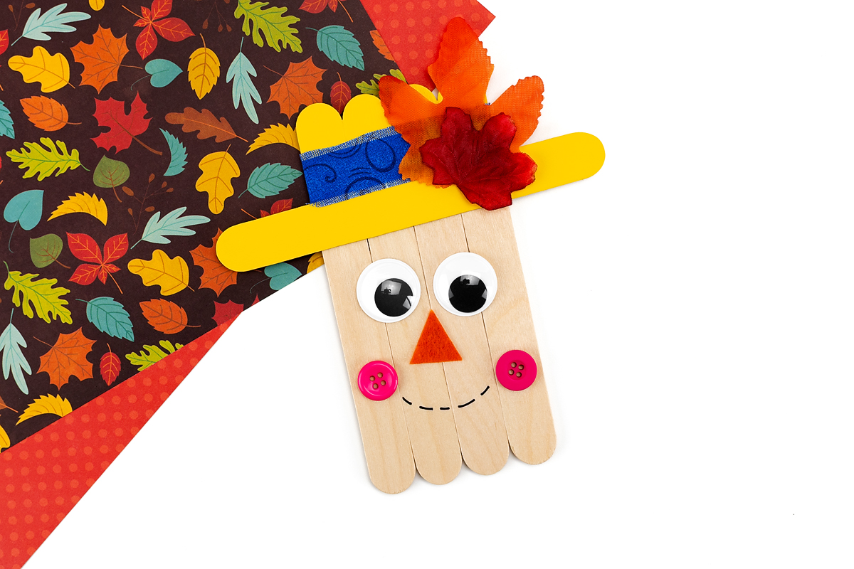 Popsicle stick scarecrow with face and decorated hat.