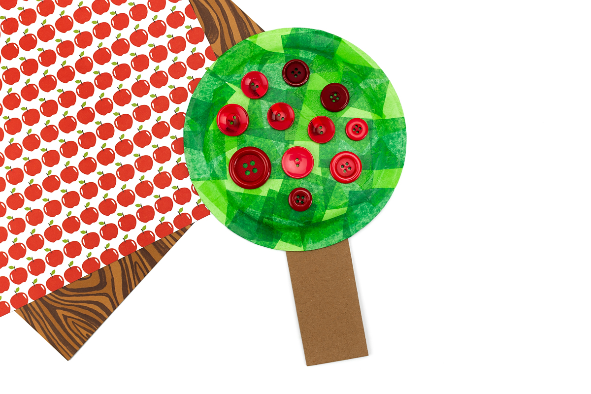 Step 4 of making a paper plate apple tree is glueing the buttons to the leaves.