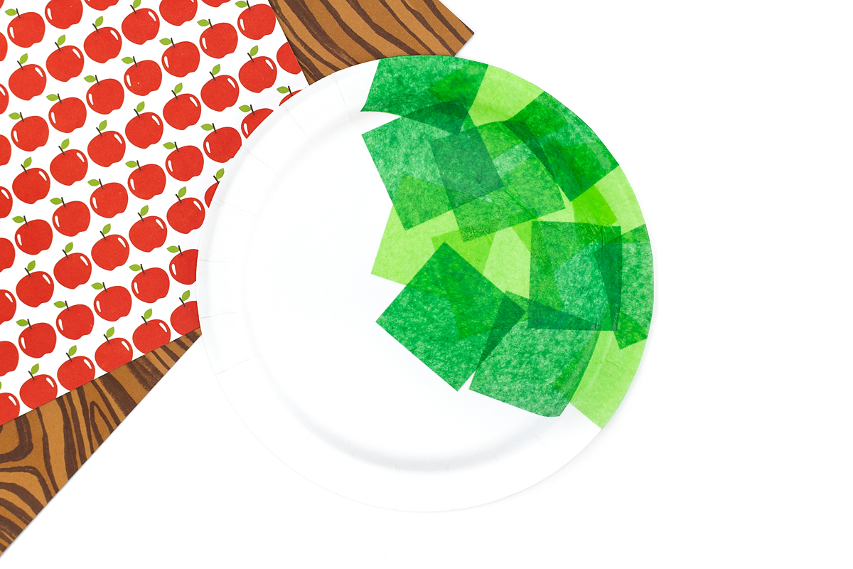 Tissue paper halfway covering a paper plate for an apple tree craft.