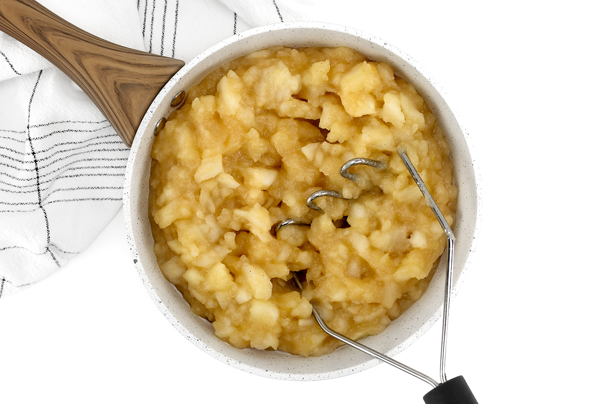 Mashing apples with a potato masher to make applesauce.