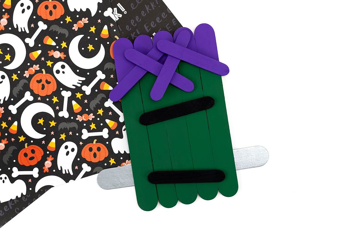 Craft stick Frankenstein with hair, mouth, bolts, and eyebrows added.