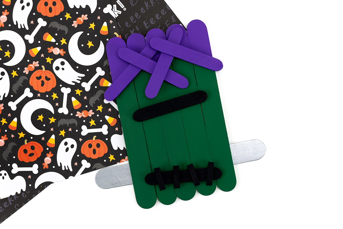 Craft stick Frankenstein with hair, mouth, bolts, stitches, and eyebrows added.