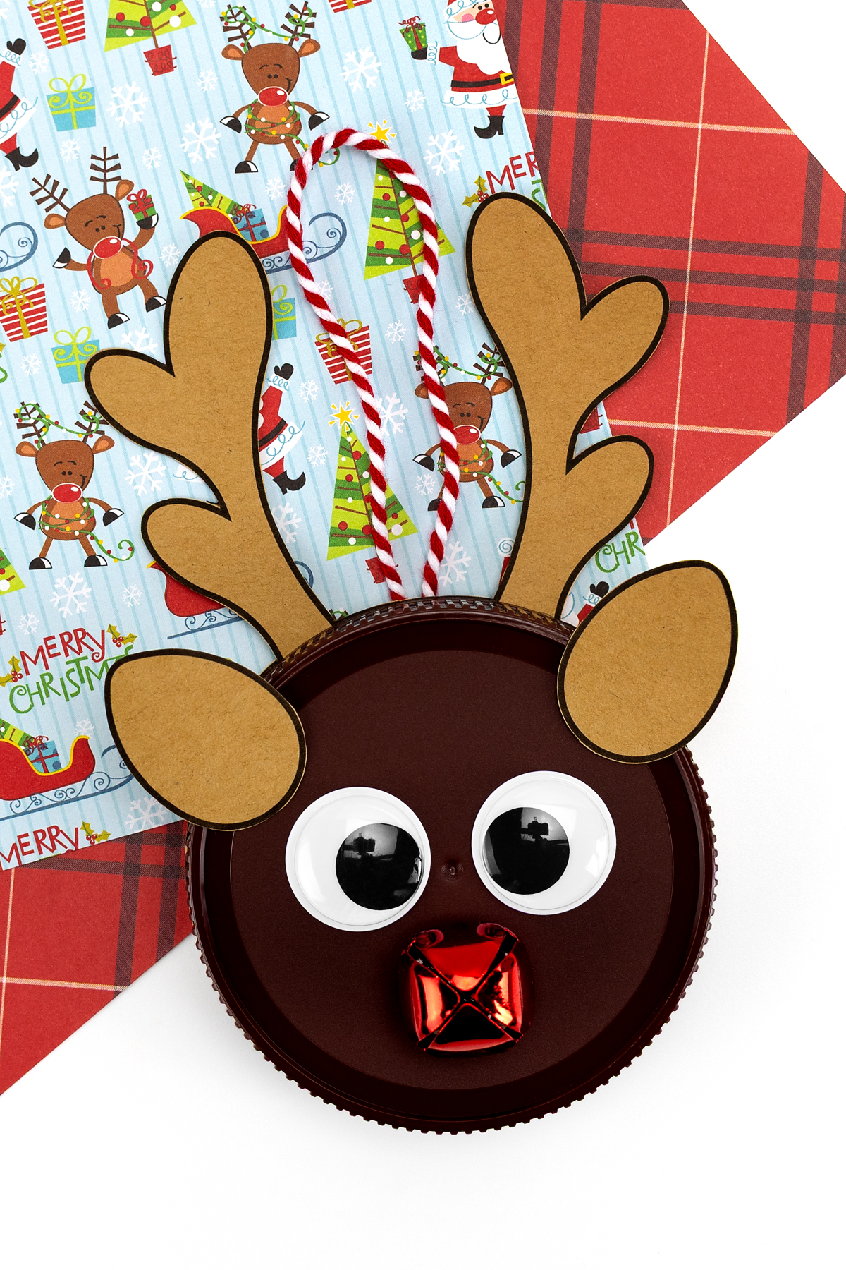 Festive reindeer ornament made from a recycled peanut butter jar lid with eyes, nose, and decorations.