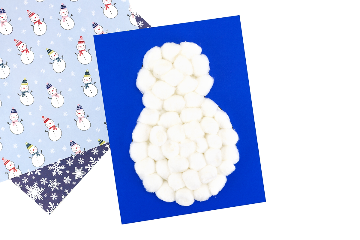 Cotton ball snowman body glued to colored cardstock, partially covered with fluffy cotton balls.