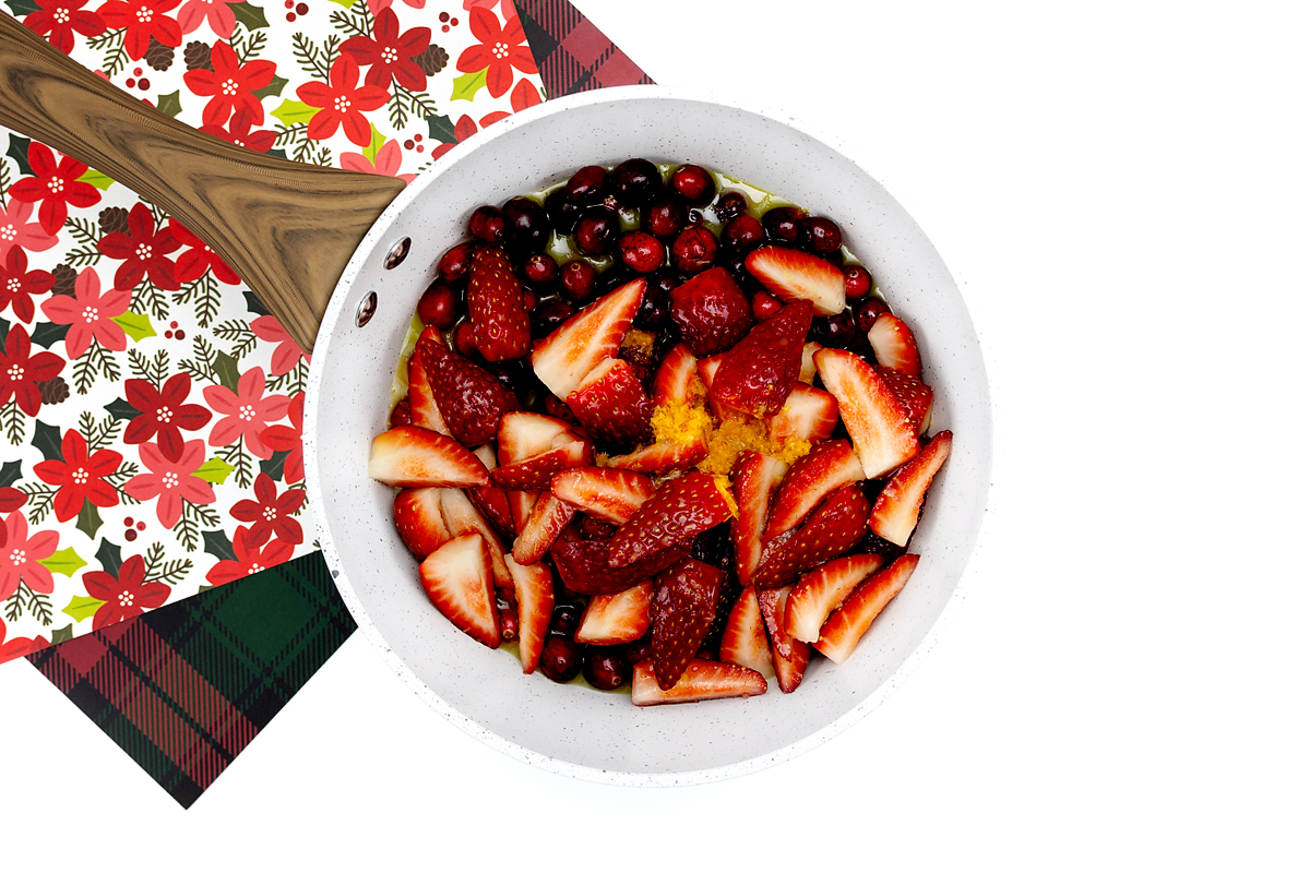 Cranberries, strawberries, orange juice, and orange zest added to a saucepan before cooking.