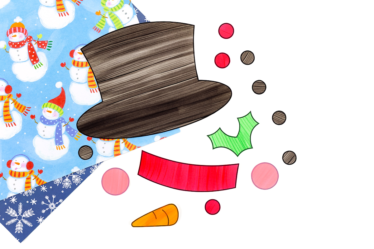 Cut-out snowman hat pieces, eyes, mouth, and carrot nose arranged on a table.