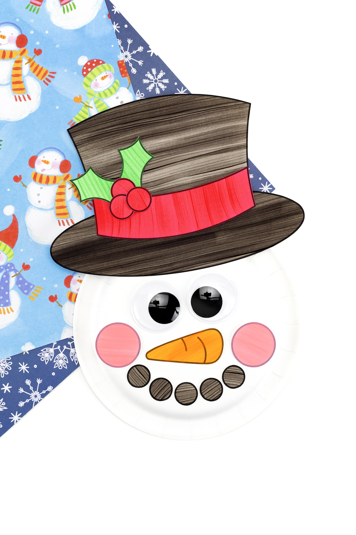 Finished paper plate snowman craft with a festive top hat and holly decoration.