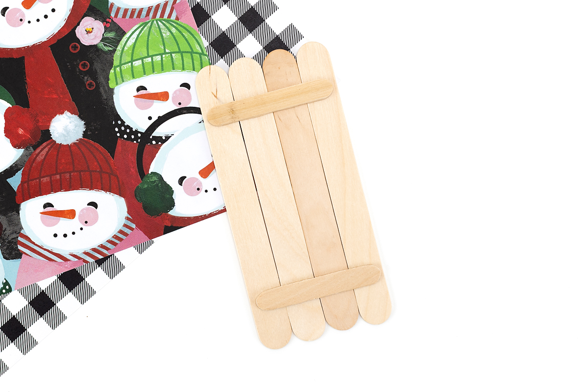 Four wide popsicle sticks glued together with two mini popsicle sticks across the back to form the snowman base.