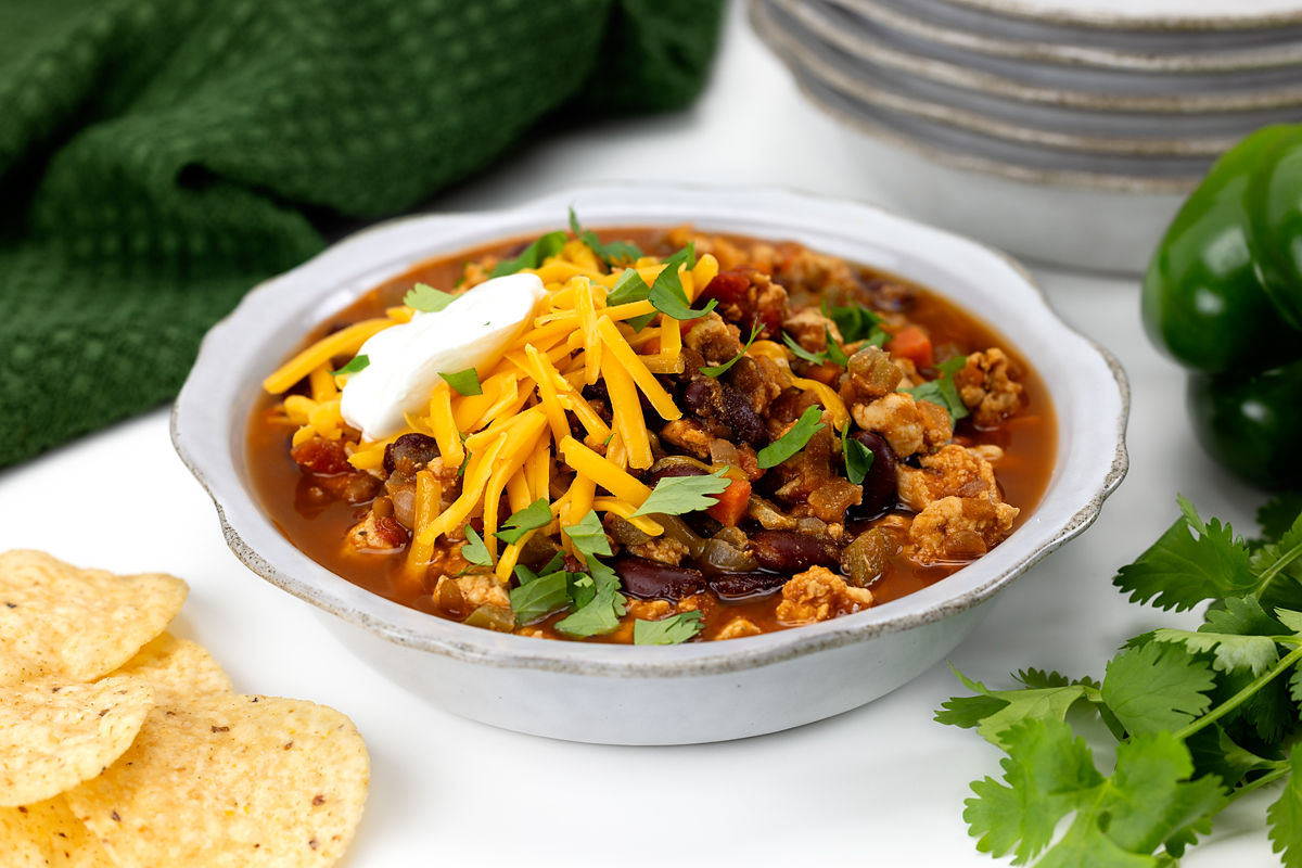 Close-up of turkey chili with lentils, kidney beans, melted cheese, and fresh herbs.
