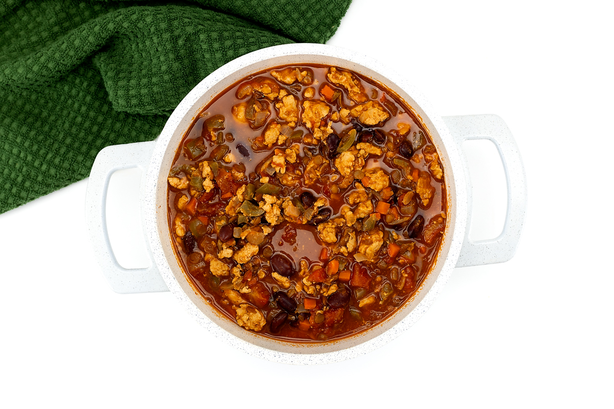 Finishing turkey chili by stirring in apple cider vinegar and adjusting seasoning.