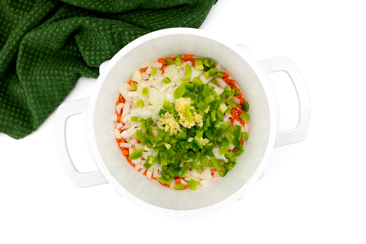 Sautéing onion, garlic, bell pepper, and carrot in a large pot on the stove.