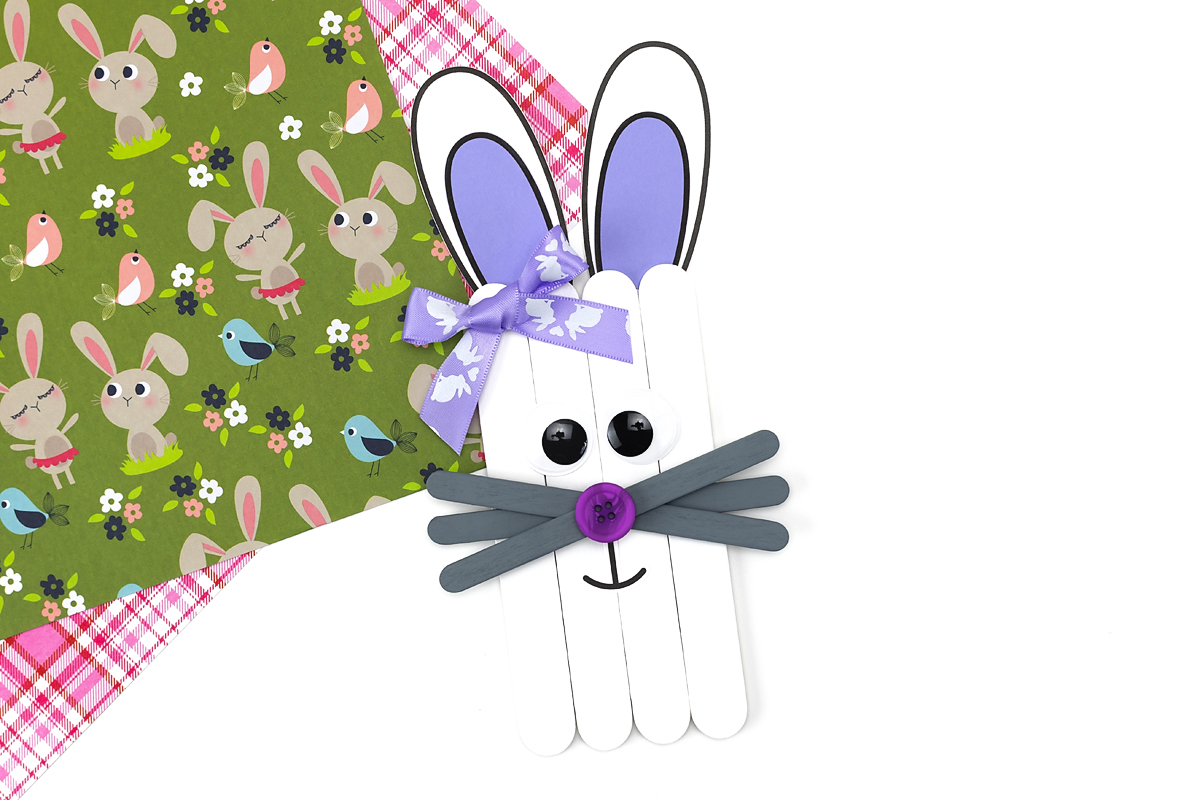 Adding eyes, nose, mouth, and a bow to complete the popsicle stick bunny craft.