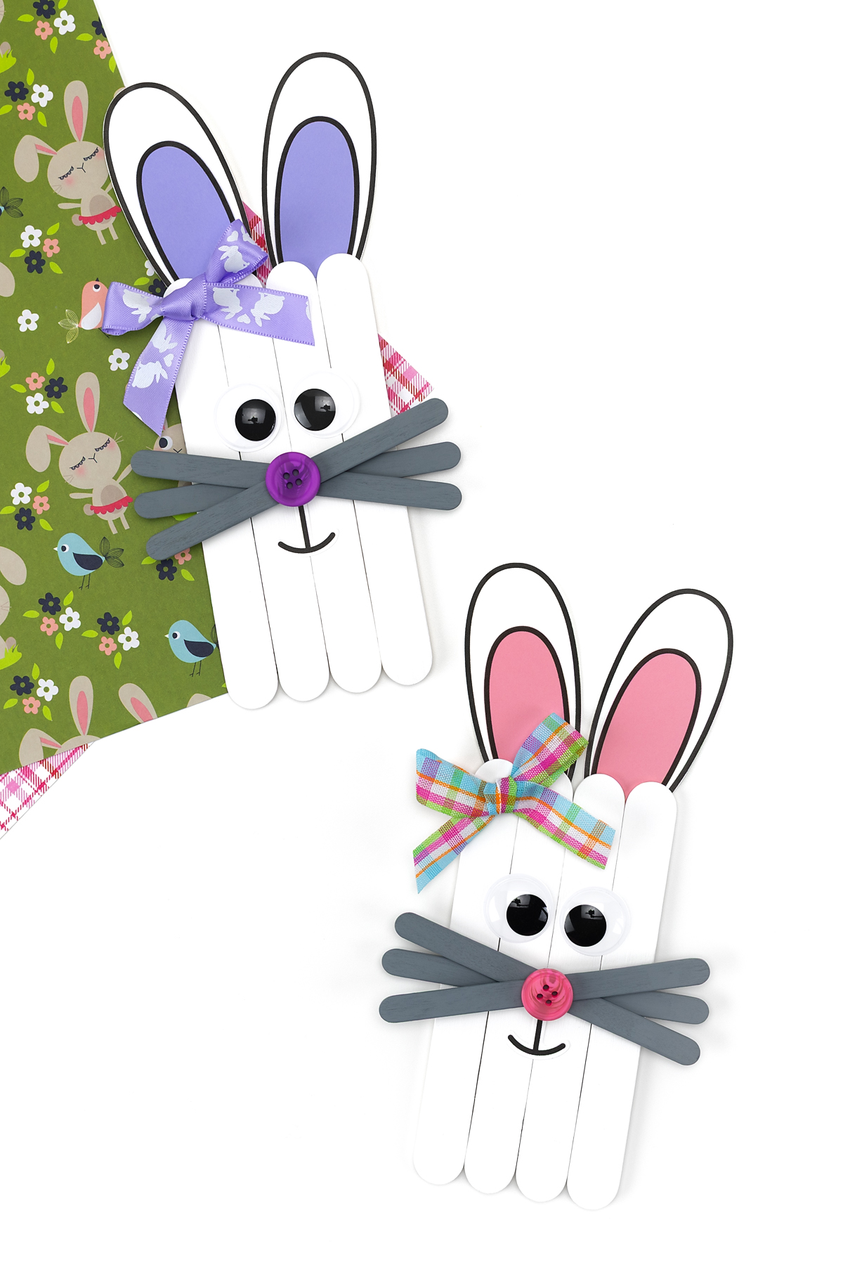 Two finished popsicle stick bunny crafts with painted faces, paper ears, and popsicle stick whiskers.