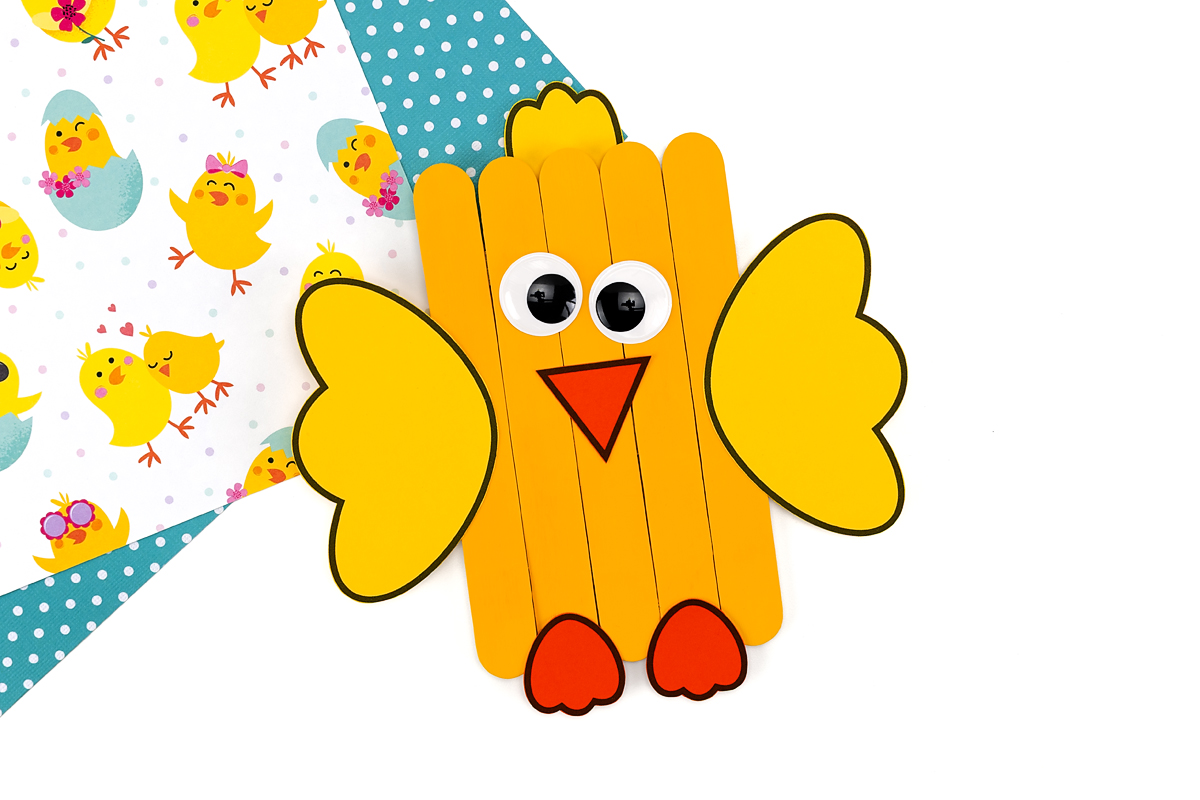 Completed chick with glued-on beak, eyes, and paper feet attached along the bottom edge of the popsicle stick body.