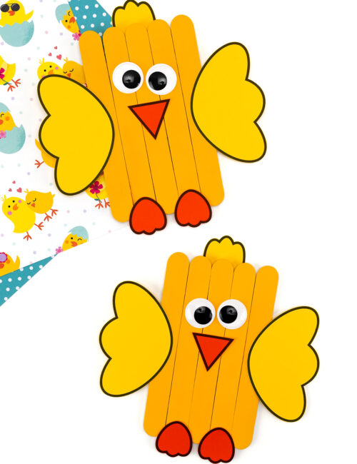 Close-up of two colorful popsicle stick chicks showing painted bodies, paper wings, tufted hair, beaks, eyes, and feet.