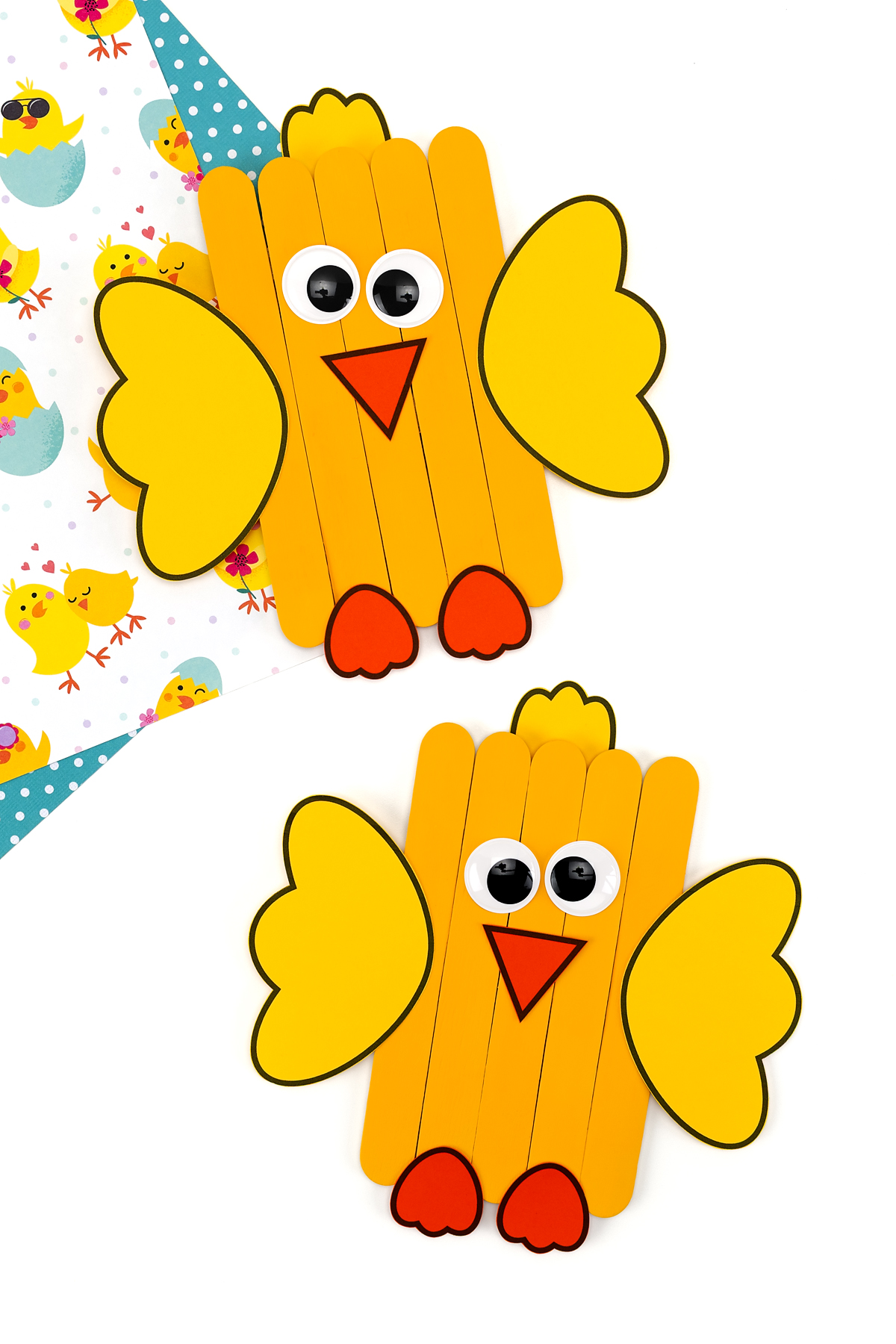 Close-up of two colorful popsicle stick chicks showing painted bodies, paper wings, tufted hair, beaks, eyes, and feet.