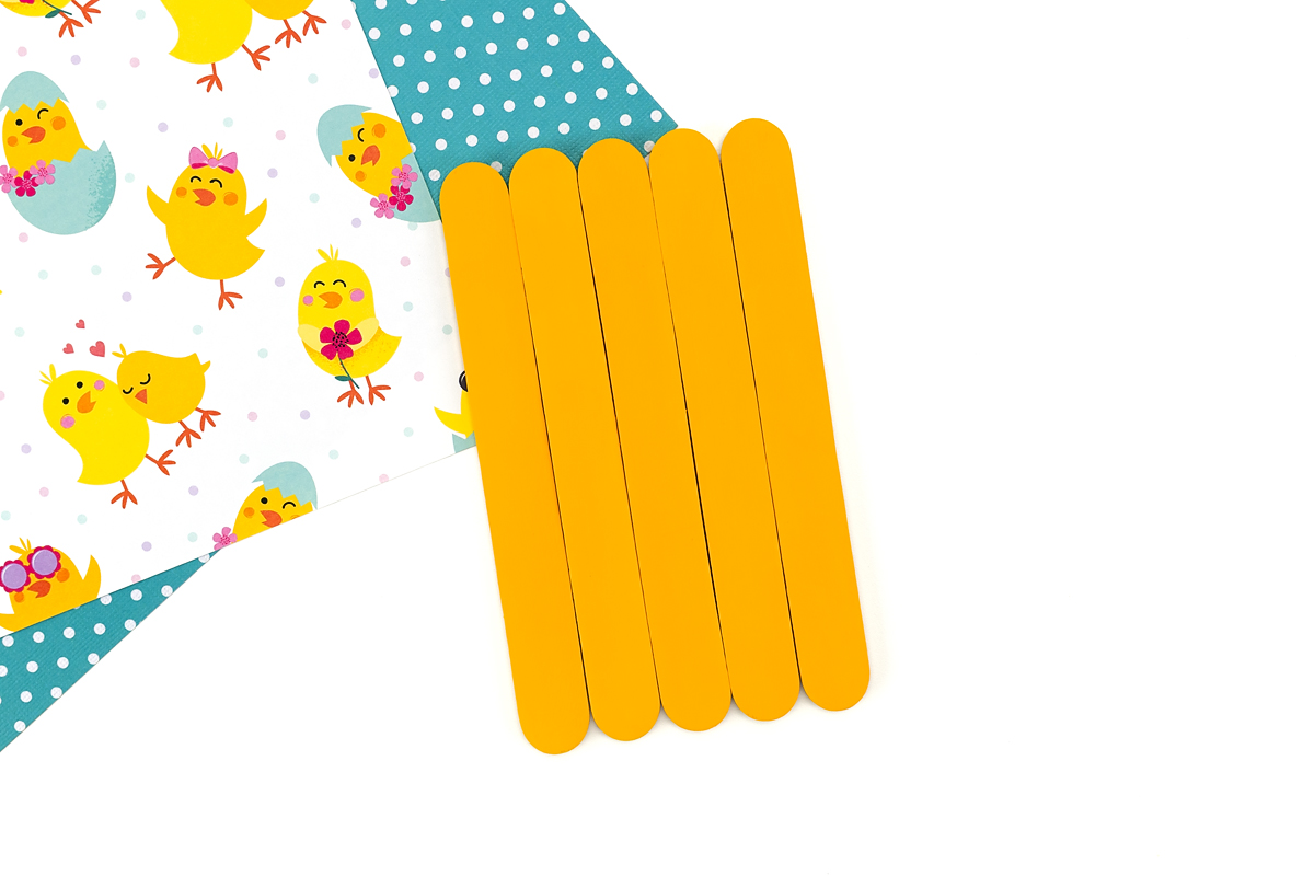 Popsicle stick chick body painted yellow with an even coat, drying on a flat surface.