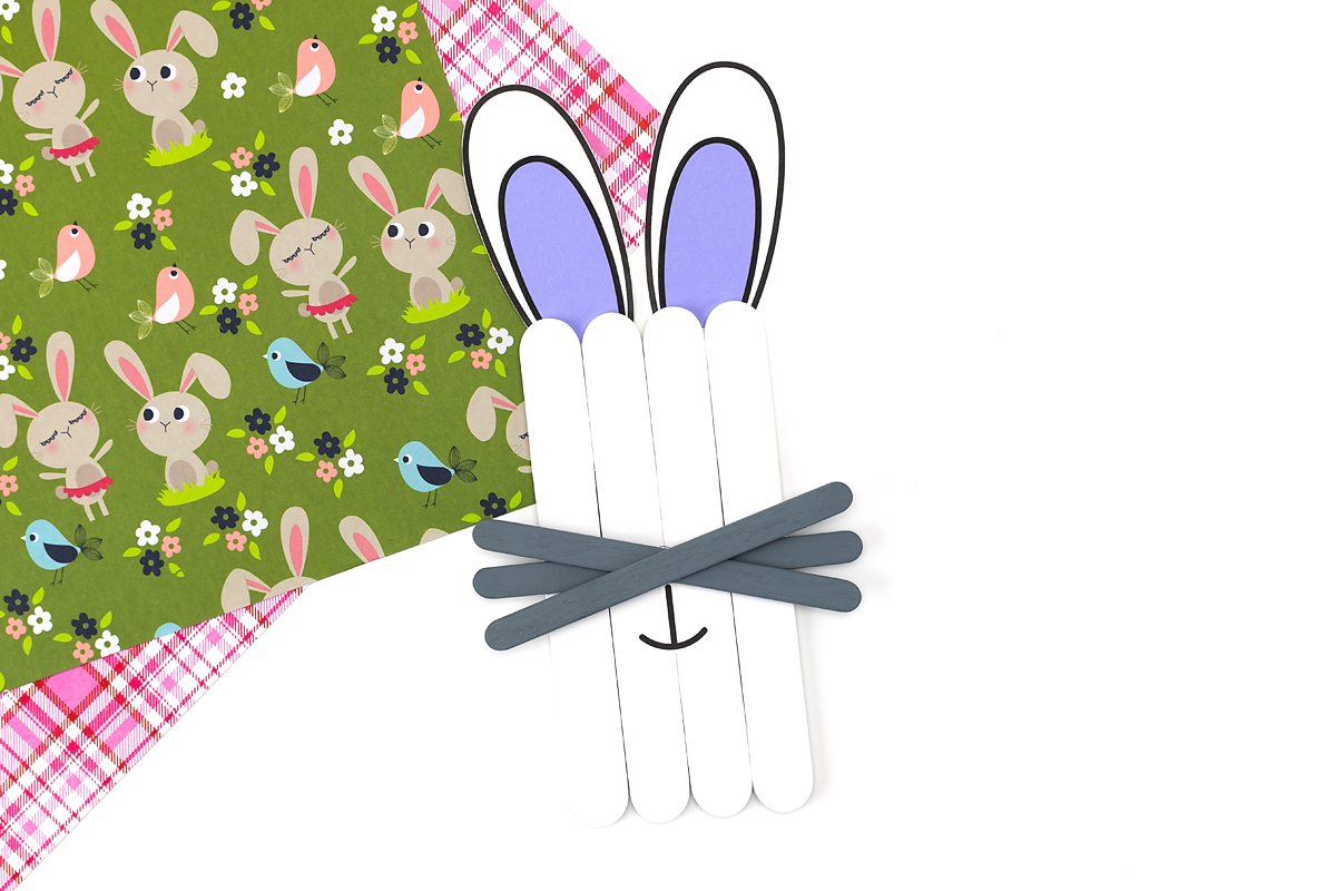 Gluing paper bunny ears to the back of the popsicle stick face so they stick out at the top.