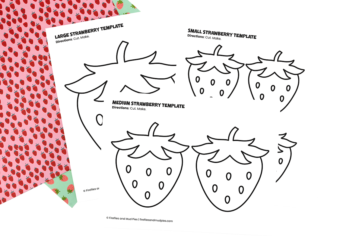 Large, medium, and small strawberry templates printed on white paper displayed on a pink and green strawberry-patterned background.