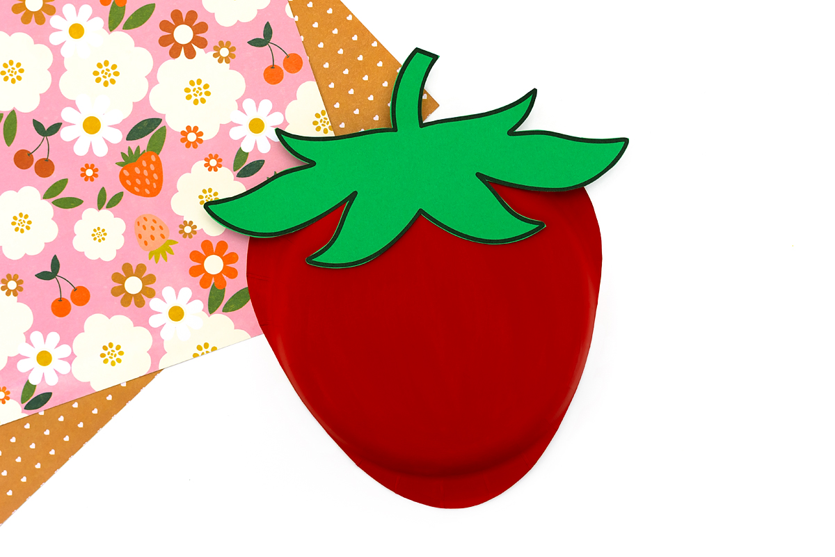Green paper leaves glued to the top of the painted paper plate strawberry.