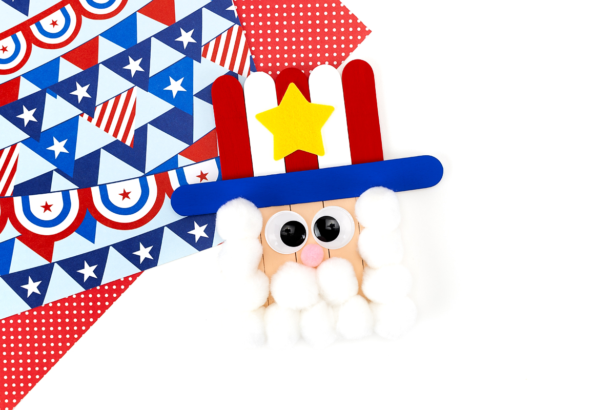Uncle Sam popsicle stick craft with wiggle eyes, pink pom pom nose, white pom pom beard, and red white and blue striped hat with yellow felt star.