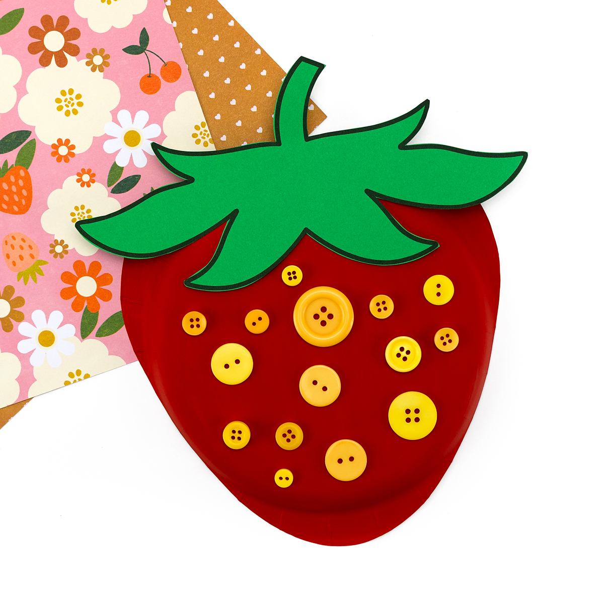 Finished paper plate strawberry craft with red paint, green leaves, and yellow button seeds.