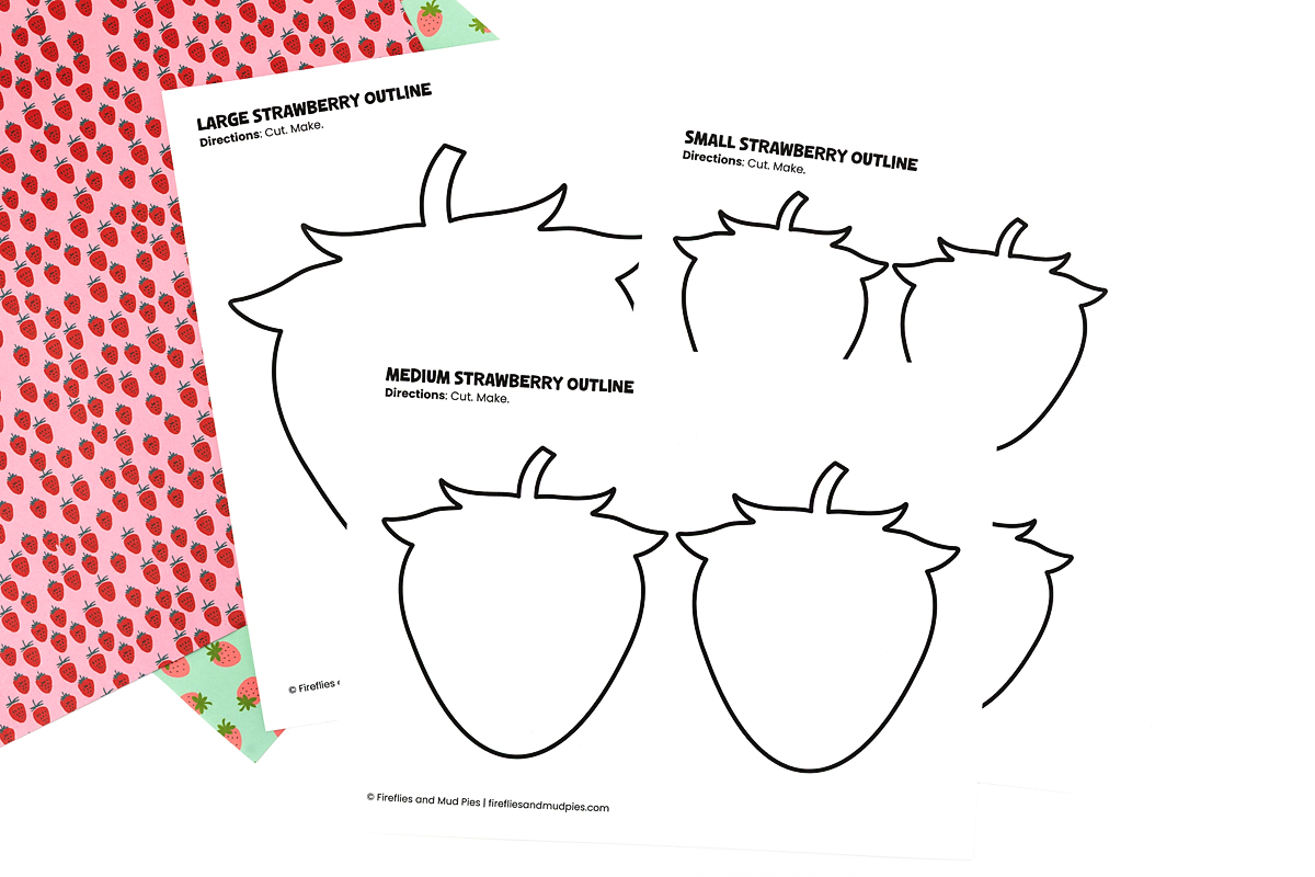 Large, medium, and small blank strawberry outline templates printed on white paper with a pink strawberry-patterned background.