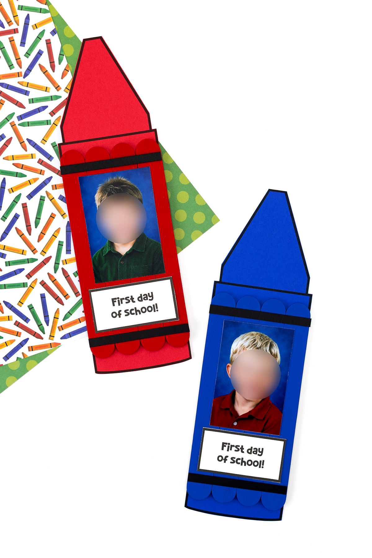 Two finished popsicle stick crayon crafts in red and blue with school photos and "First Day of School" labels, displayed vertically on a colorful crayon-print background.