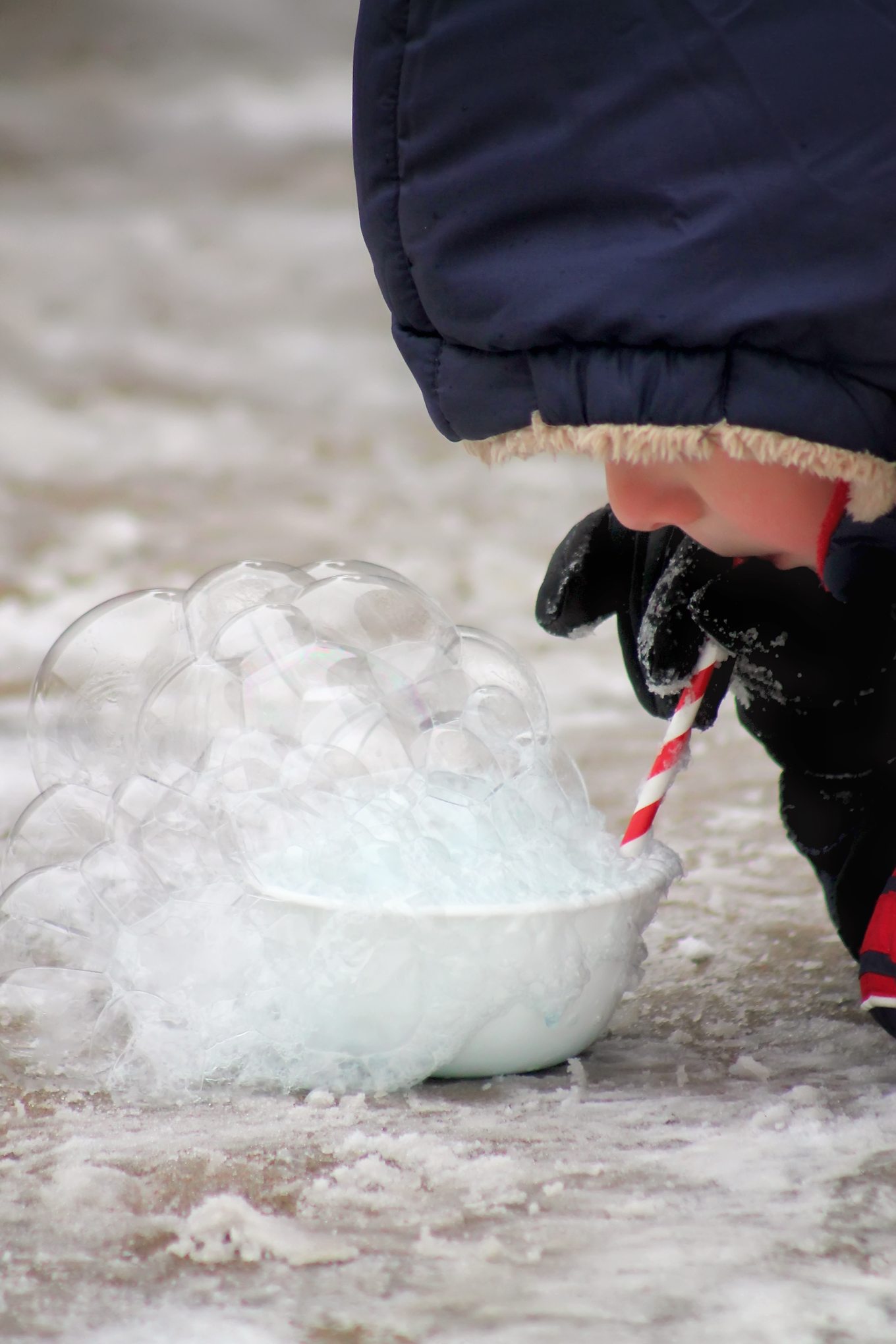 Child Blowing Bubbles Through a Straw in Winter